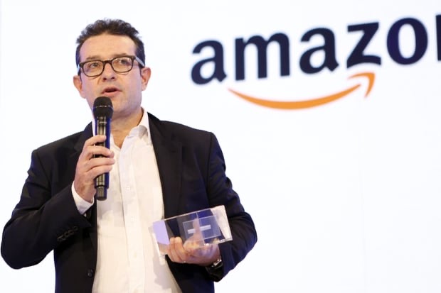 Hugues Pitre sur scène, micro à la main, devant le logo Amazon