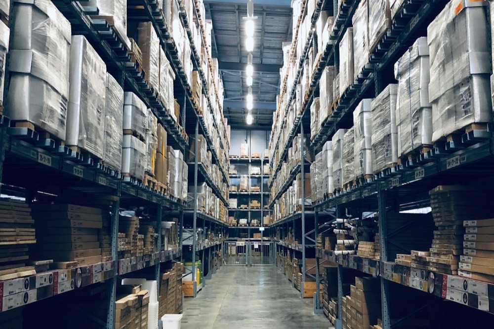 Allée d'entrepôt logistique en perspective, racks chargés de palettes filmées de part et d'autre